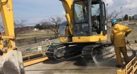 洗車員が高圧洗浄機で重機のキャタピラーの泥を落としています。