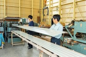 製造：ロール成型機から出てきた外壁材を受け取っています