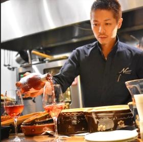 オープンキッチンでカウンターのお客様へワインをサーブ