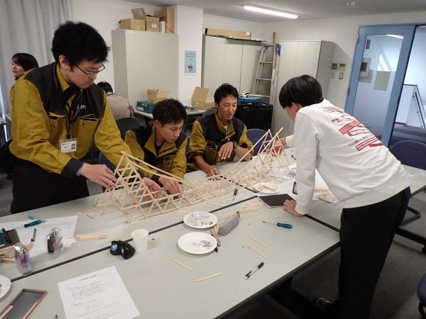 新入社員研修では、中途社員と共に和気あいあいと研修します。写真は設計部の研修の中で、アイス棒を使用した強度の高い橋を作成している様子です。