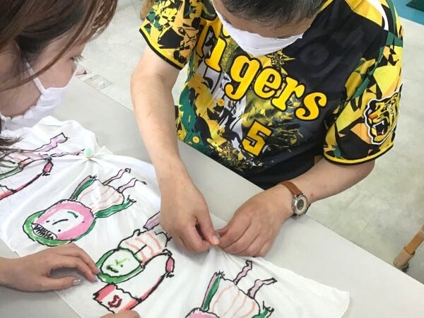 商品製作の一コマ。印刷が完成した手ぬぐいに染色のための絞り加工を行っています。