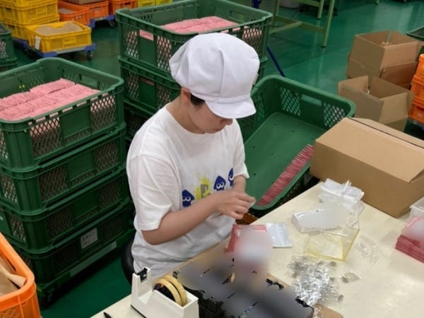 梱包作業風景です。紙袋にキーホルダーとボールチェーン、注意書きの紙を入れています。（注：本画像は青梅工場）