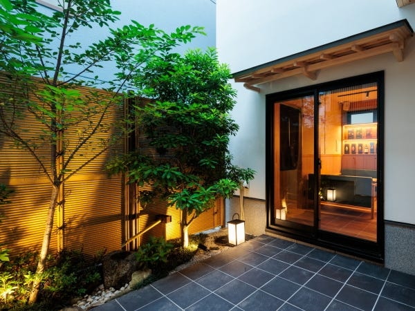 緑豊かな木々をあしらった、洗練されたバーの入り口。自然の息吹と都会のエレガンスが融合した、隠れ家のような空間へ